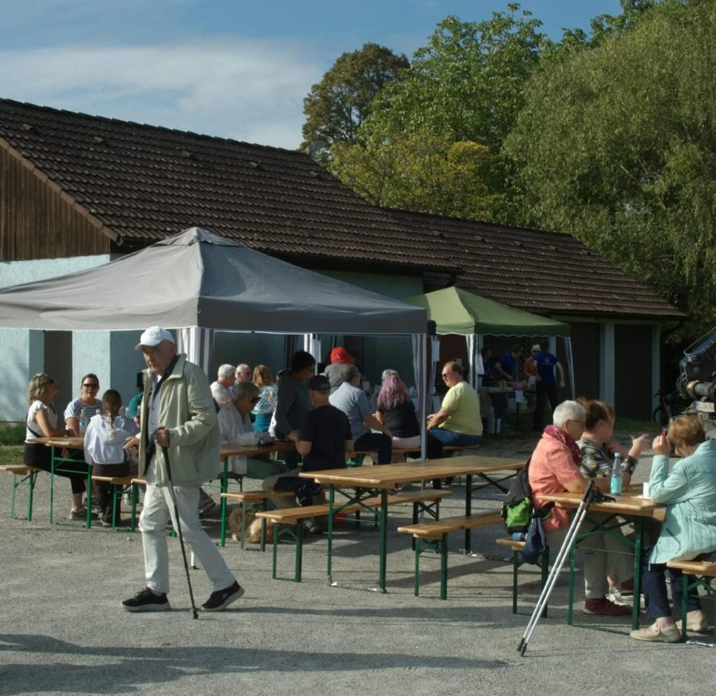 Gäste sitzen bei sonnigem Wetter an Bierbänken vor der Remise auf dem Festplatz Völkersbach